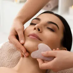 Relaksacyjny masaż twarzy z użyciem kamienia gua sha. Kobieta z zamkniętymi oczami doświadcza odprężenia podczas zabiegu.