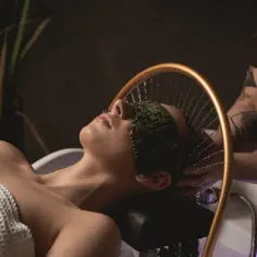 Relaks w domowym spa: delikatne krople wody spływają po twarzy kobiety z kamienną maską na oczach.