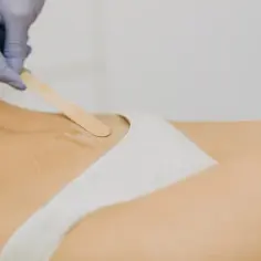 Ręka w rękawiczce nakłada wosk na skórę, przygotowując do depilacji woskiem w domu.